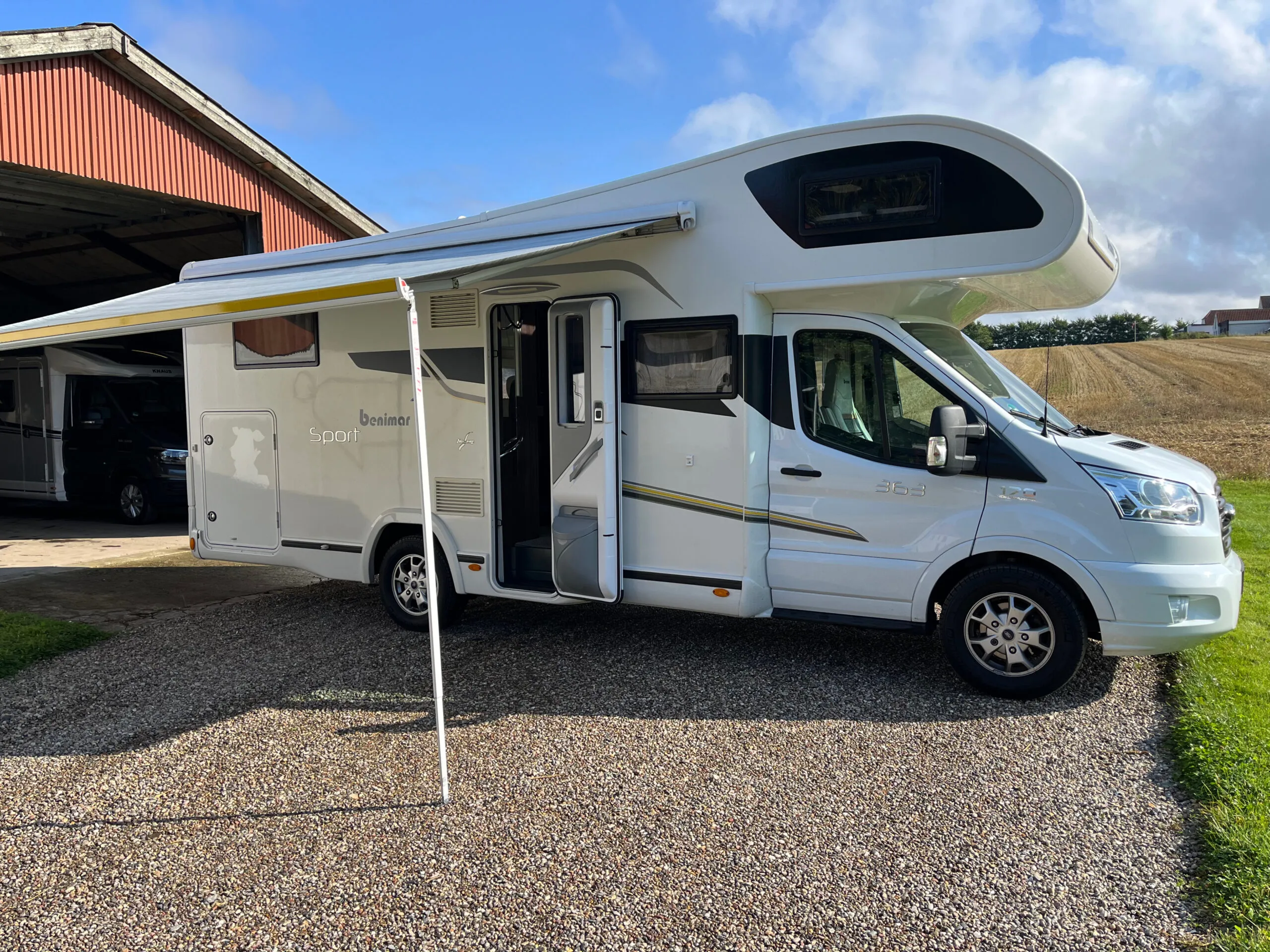 Hvid autocamper med markise ved landejendom